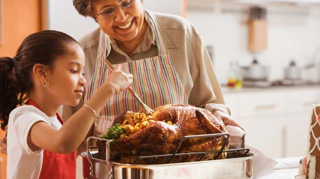 Grandmother and granddaughter smiling and basting turkey