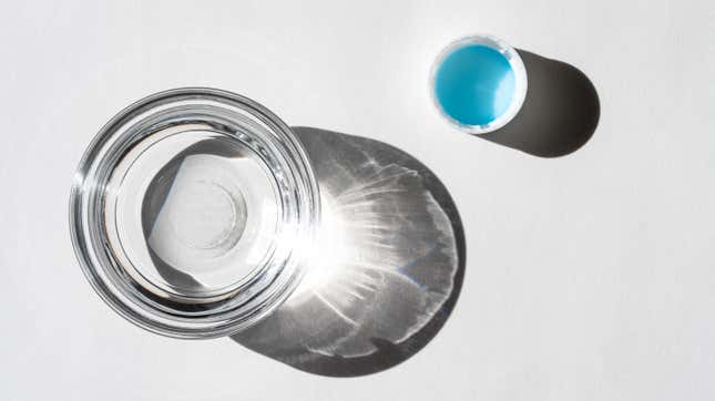 A small clear glass bowl of distilled white vinegar and an upturned plastic bottle cap with a blue liner sit on a white background.