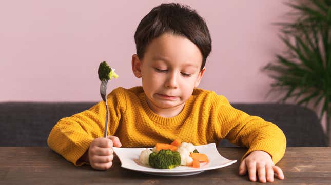 Young boy looking disgusted at plate of vegetables