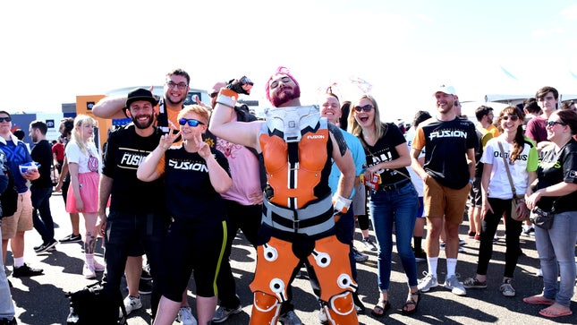 Fans stand outside the venue for the 2src19 OWL Grand Finals, some wearing Philadelphia Fusion shirts. A Zarya cosplayer stands in the center.