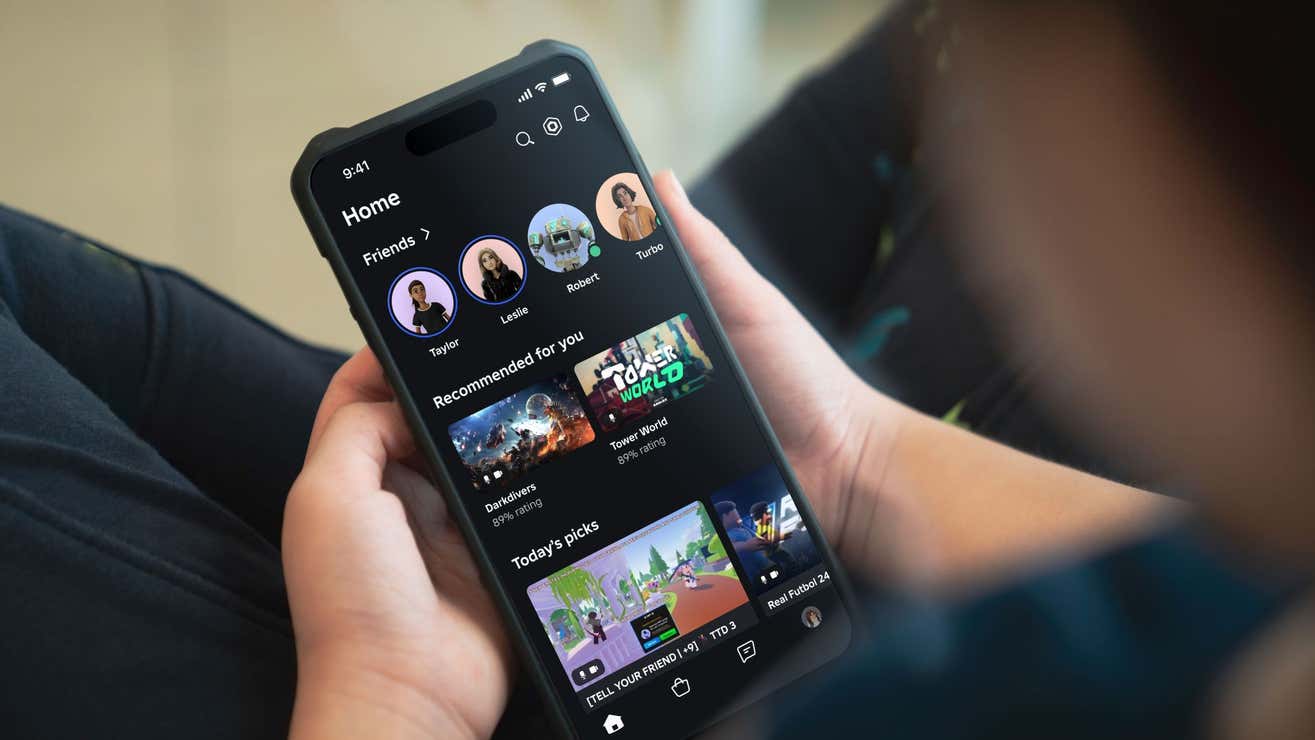 Un usuario que sostiene un smartphone que muestra la pantalla principal de la aplicación de Roblox. En la interfaz se pueden ver las fotos de perfil de amigos en la parte superior, junto con una sección de juegos recomendados, como "Darkdivers" y "Tower World", y una lista de selecciones del día con juegos destacados. El diseño de la app tiene un fondo oscuro con texto y gráficos coloridos que resaltan las opciones.