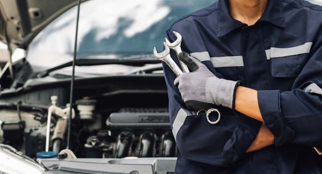 Mechanic holding two wrenches in front of a car with the hood up