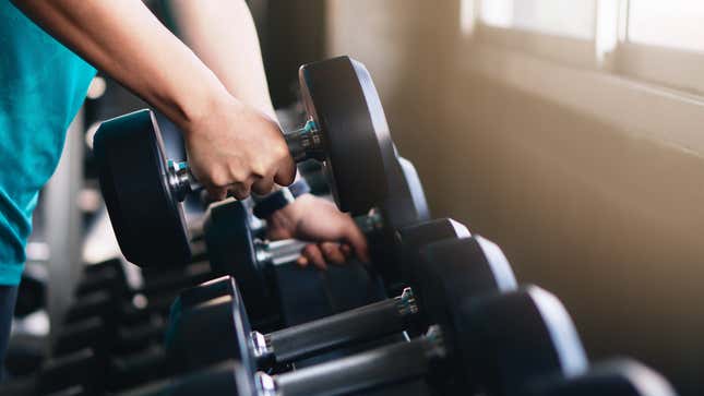 hands of man lifting dumbbells on rack in gym or fitness