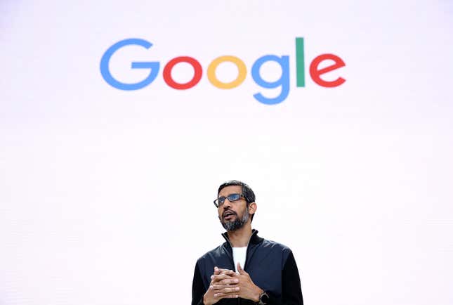 vue vers le haut de Sundar Pichai parlant avec ses mains jointes sous un logo Google coloré sur un fond blanc