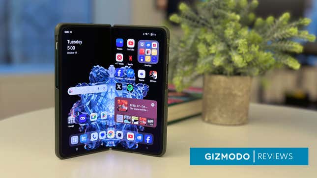 A OnePlus Open foldable phone with a green back in front of a fake potted plant and book.