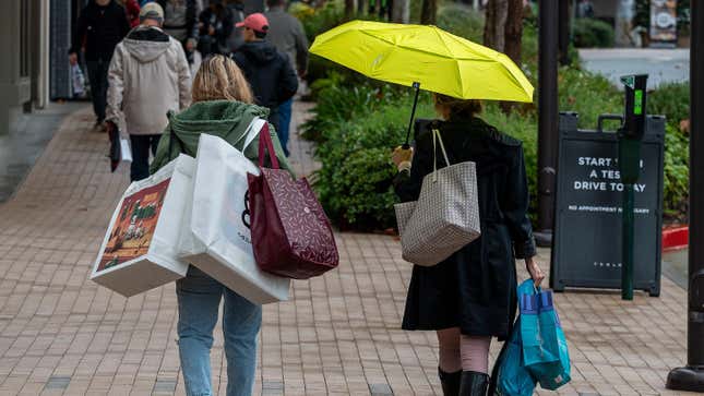 Shoppers carrying shopping bags at an outdoor shopping center.