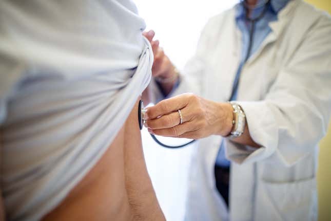 Medical professional checking woman's back with stethoscope in clinic