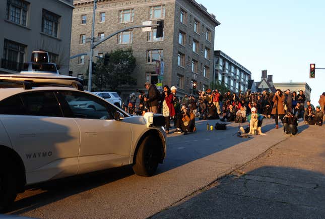 A group of people stand in front of a self-driving car at sunrise in San Francisco. 