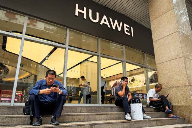 Personas sentadas en los escalones de afuera de una tienda Huawei mirando y hablando por sus teléfonos