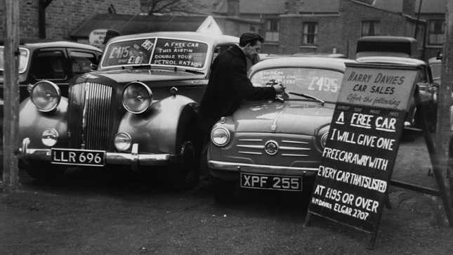 A black and white photo of a vintage car dealer with two models on the lot. 