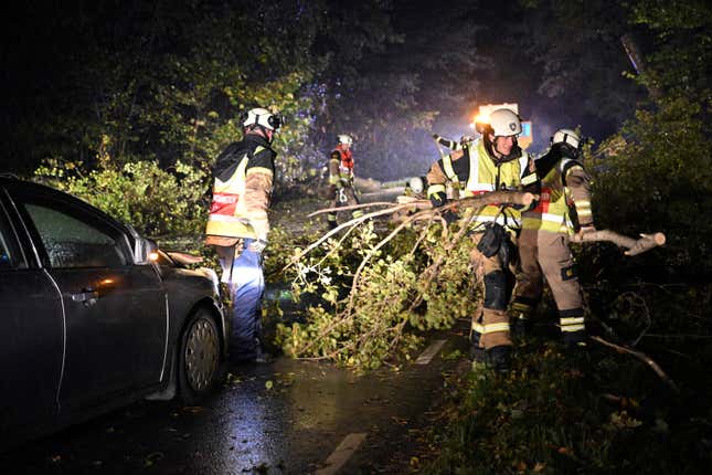 The emergency services clear away fallen trees that hit a car and block a road outside Lund, southern Sweden, on Friday, Oct. 20, 2023, as storm Babet moved in over the region. Gale-force winds and floods have struck several countries in northern Europe as the region endures more heavy rain that forecasters say will continue into the weekend. (Johan Nilsson/TT News Agency via AP)