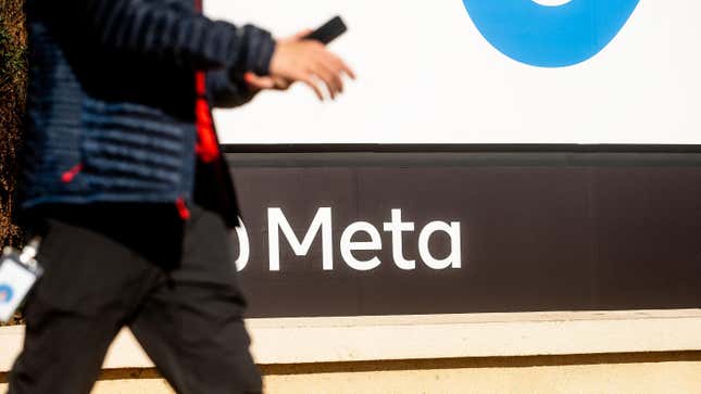 A man on his phone walks in front of the Meta logo 