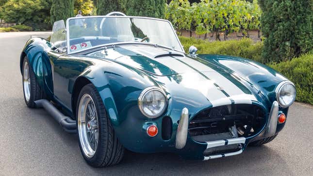 Una réplica de un Shelby Cobra verde con rayas blancas estacionada frente a unas plantas