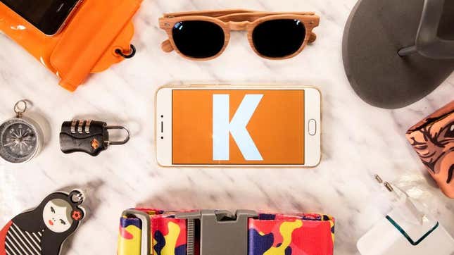 The Kayak logo on a phone surrounded by travel-related objects