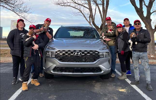 Silver Hyundai Santa Fe surrounded by people in red hats holding beagle dogs.