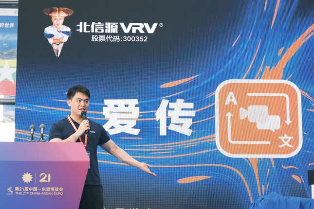 man on stage speaking in a microphone in front of a display of the AITran tool