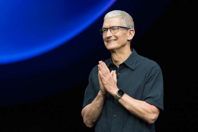 Tim Cook (in a green, short-sleeve button-down) clasps his hands together as he stands on stage