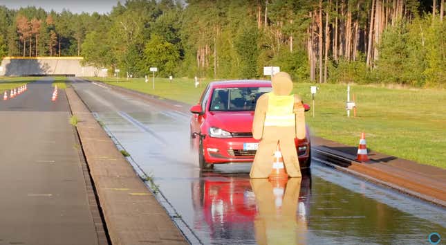 A red Volkswagen Golf is about to hit a foam human crash dummy on a wet track.