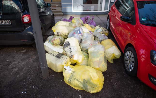 Numerous garbage bags lie between parked cars along a road.