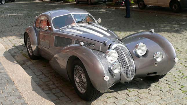 A photo of a retro-styled sports car parked on a cobbled street. 