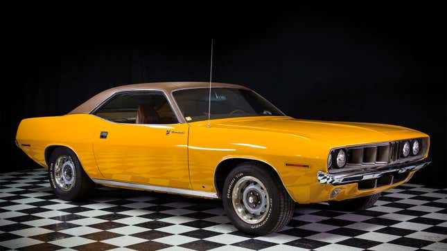 A photo of a yellow Plymouth Barracuda in a studio. 