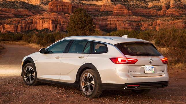 Un Buick Regal Tour X blanco estacionado sobre tierra frente a las montañas