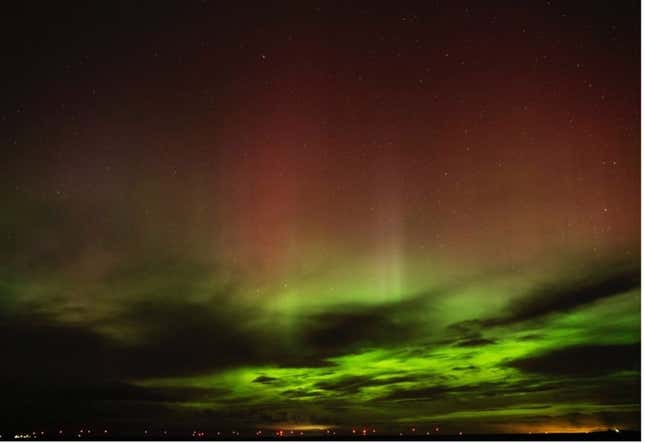 An aurora lights up a cloudy sky in shades of bright green