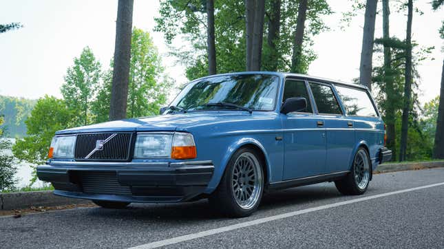 A front 3/4 shot of the scotia blue Volvo 240 in front of trees