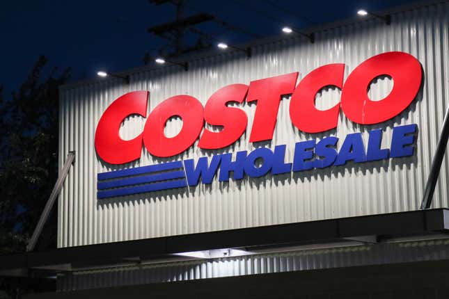 un panneau Costco (rouge) Wholesale (bleu) à l’extérieur d’un bâtiment la nuit