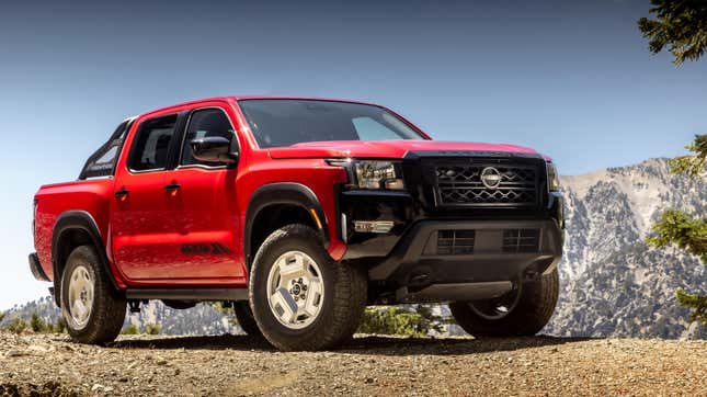 A red Hardbody-style Frontier parked on dirt in front of mountains