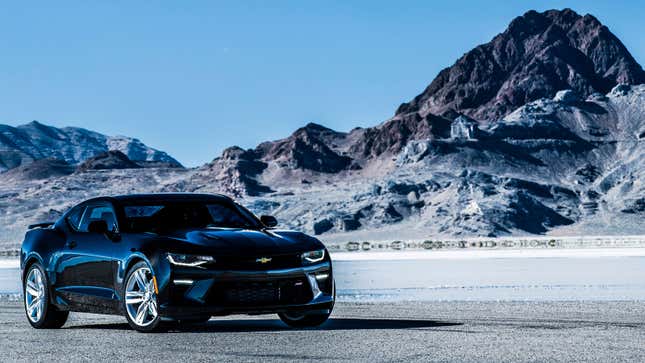 A photo of a dark blue Camaro muscle car parked in front of a mountain. 