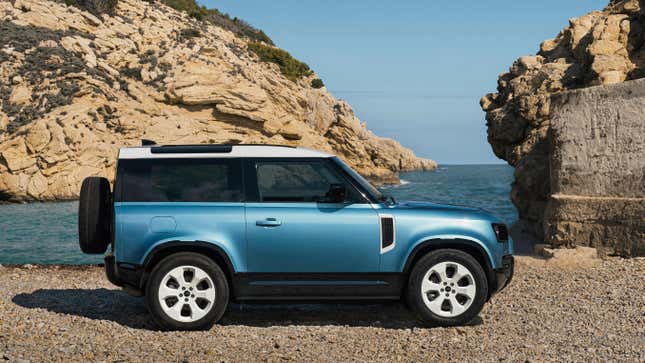 Vue latérale d’un Defender 90 bleu stationné sur une plage devant des rochers