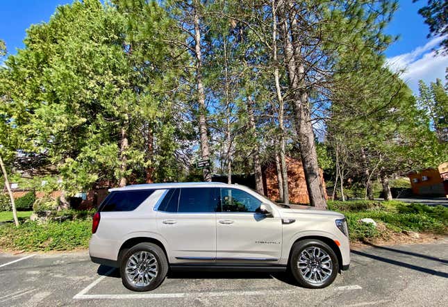A side view of the beige Yukon parked in front of some trees