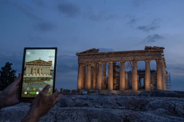 A man holds up a tablet showing a digitally overlayed virtual reconstruction of the ancient Parthenon temple, at the Acropolis Hill in Athens, Greece on Tuesday, June 13, 2023. Greece has become a late but enthusiastic convert to new technology as a way of displaying its famous archaeological monuments and deepening visitors&#39; knowledge of ancient history. The latest virtual tour on offer is provided by a mobile app that uses Augmented Reality to produce digital overlays that show visitors at the Acropolis how the site and its sculptures looked 2,500 ago. (AP Photo/Petros Giannakouris)