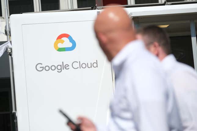 Two out-of-focus people in white shirts stand in front of a large Google Cloud sign