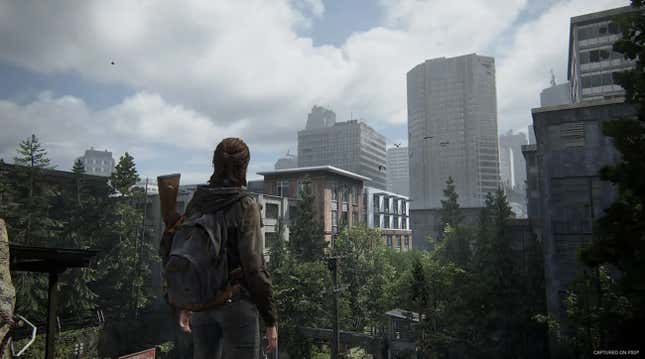 Ellie looks at a skyline on an overgrown city street in a moment from The Last of Us Part II.