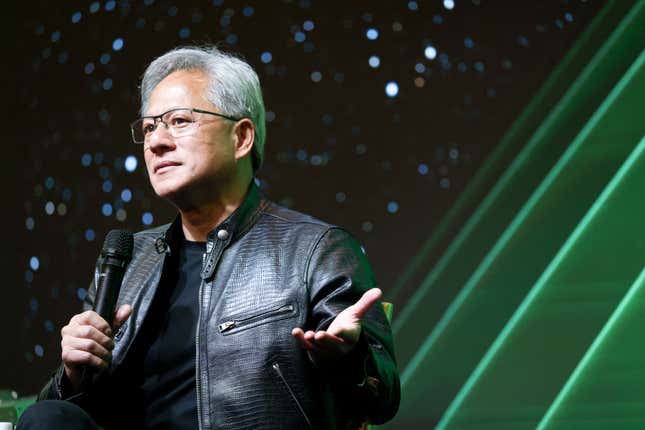 jensen huang holding a microphone in one hand and gesturing with the other while wearing a leather black jacket in front of a backdrop that looks like a starry black sky with beams of green light