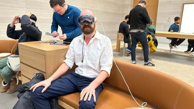 A person in a white shirt and pants wearing a Vision Pro with the cord attached to the headset.