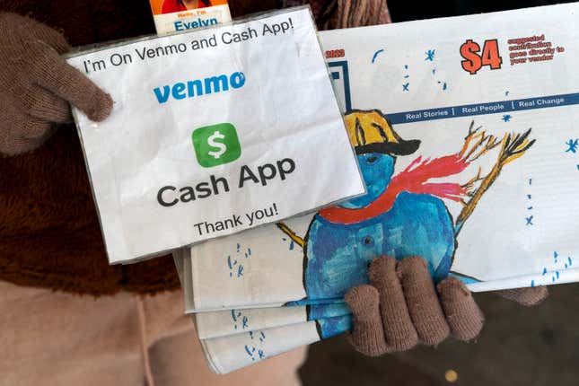 A vendor selling Street Sense, a local paper that covers issues related to the homeless and employs unhoused individuals as its vendors, holds up her sign saying she can accept donations from cashless apps like Venmo and CashApp, Wednesday, Dec. 6, 2023, in Washington. The transition to a cashless society has impacted street-level charitable giving – from individual donations to panhandlers to the Salvation Army donation kettles. (AP Photo/Jacquelyn Martin)