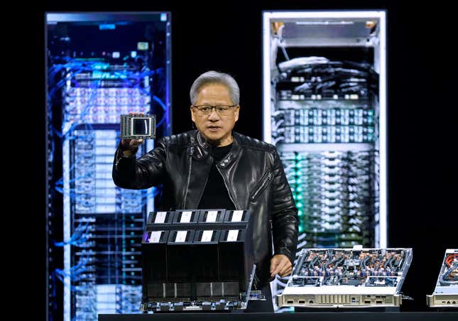 Jensen Huang holding up a chip behind other chip platforms in front of a backdrop with illustrations of server racks