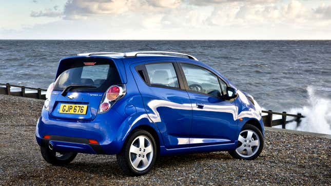 A photo of a blu Chevrolet Spark parked on a beach. 