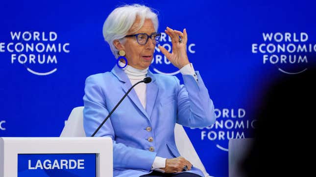 Christine Lagarde sits on a panel at the World Economic Forum with one hand raised near her glasses