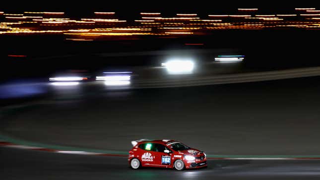 A photo of a red car racing round a circuit at night. 