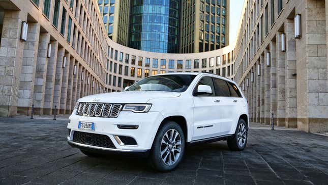 A photo of a white Jeep Grand Cherokee SUV parked by a building. 