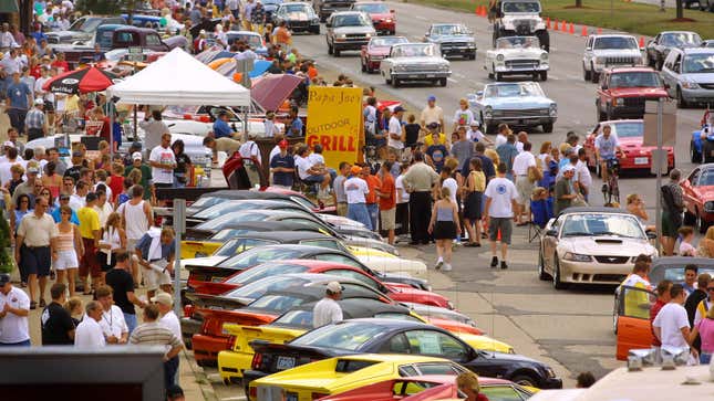 A photo of crowds of people walking around parked cars at a big car show. 