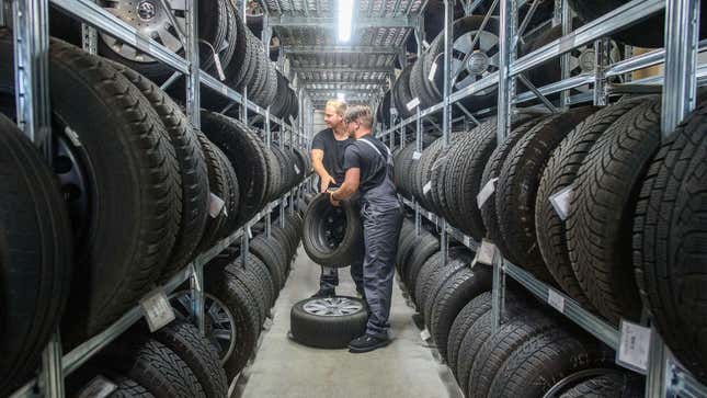 A photo of two men taking car wheels off a shelf. 