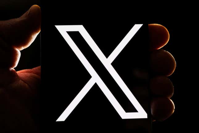 X logo displayed on a smartphone, a darkly backlit hand is holding the phone