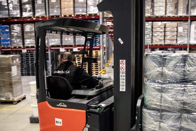 A person operating a forklift in a warehouse moving large quantities of things