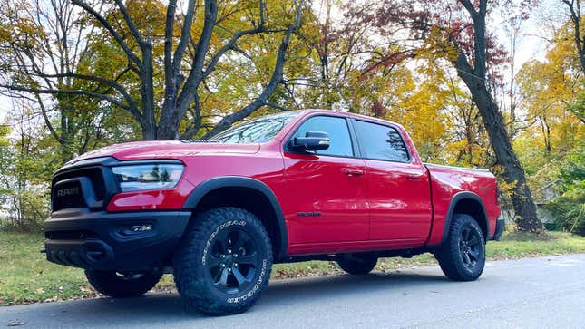 Red Ram 1500 Rebel truck with full cab and short bed, stopped on a street with colorful fall trees behind it