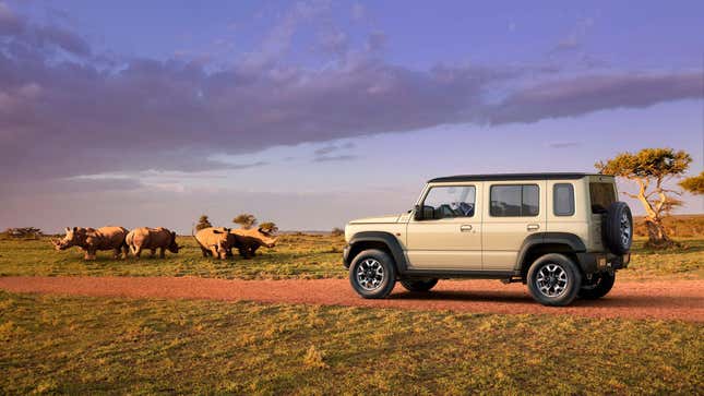 A tan Jimny Nomade parked on dirt in front of rhinos 